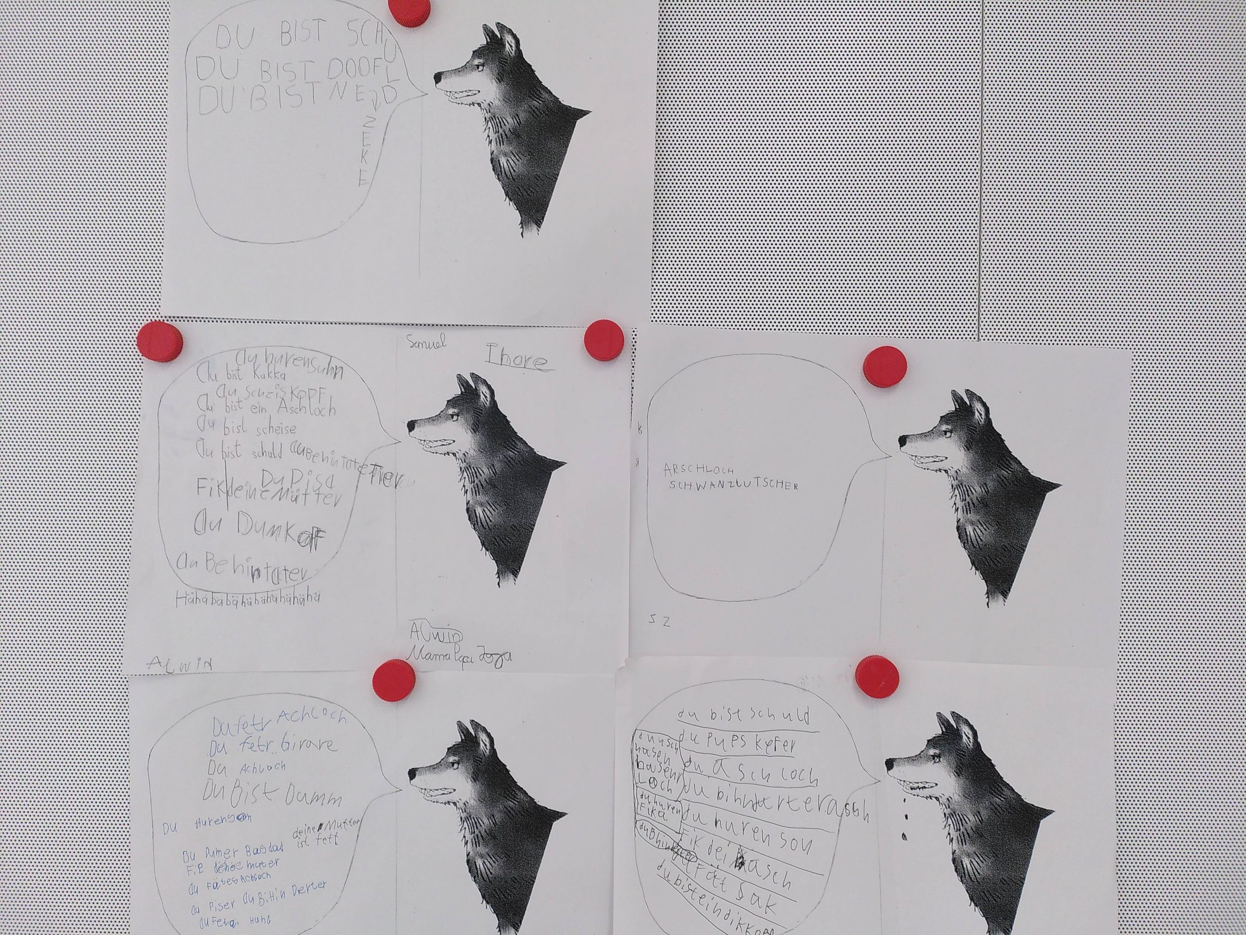 sechs schwarz weiße arbeitsblätter mit wolfsillustrationen sind an eine tafel gepinnt. jedes blatt enthält handgeschriebenen deutschen text in und um sprechblasen, die an den wolf gerichtet sind. vier rote stecknadeln halten die blätter an ihrem platz.