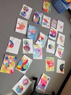 Unser Wasser-Projekt bunte kinderkunstwerke, darunter abstrakte gemälde und farbraddesigns, sind auf dem grauen boden verstreut angeordnet.