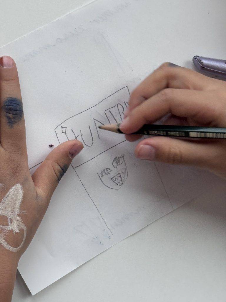 KPop Demon Hunters die hände eines kindes zeichnen mit einem bleistift auf weißes papier. die zeichnung scheint ein gesicht unter dem wort hunter zu sein. auf der linken hand und den fingern des kindes sind kritzeleien zu sehen.