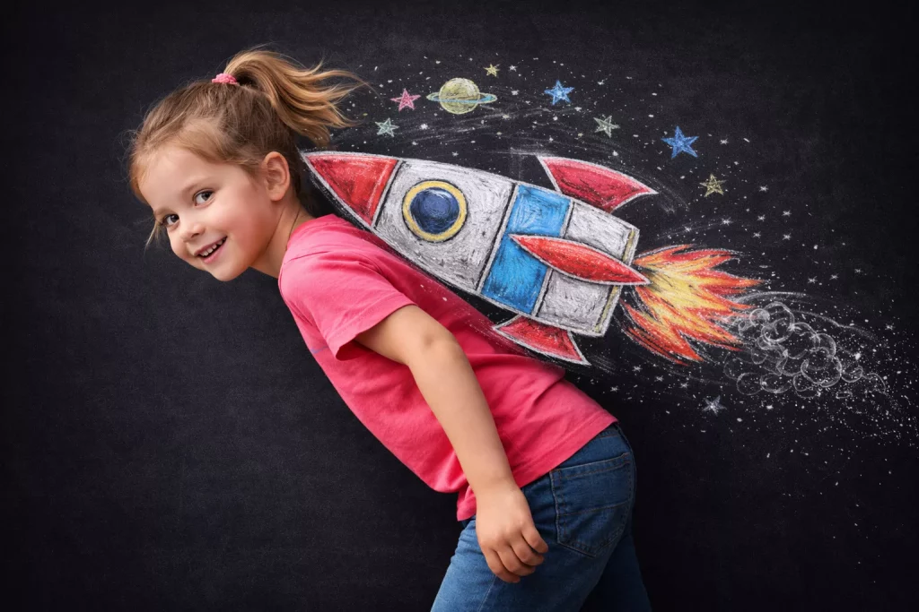 ein lächelndes junges mädchen in einem rosafarbenen hemd posiert vor einer tafel mit einer bunten kreidezeichnung einer rakete, sternen und planeten, so dass es aussieht, als würde sie mit der rakete auf dem rücken ins all fliegen.