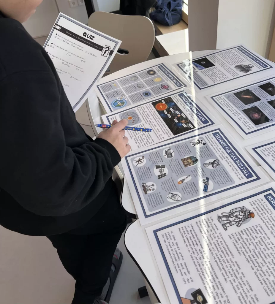 eine person steht an einem tisch, liest gedruckte wissenschaftliche informationsblätter und hält ein quiz mit einem bleistift in der hand, so als würde sie eine bildungsaktivität durchführen.